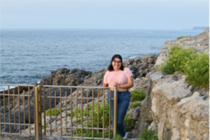 A student in a pink top and blue jeans poses for a photo in front of a cliff in Spain.