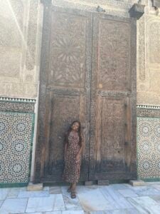 Student standing confidently in front of a grand and historic door of Al-Qarawiyinn University