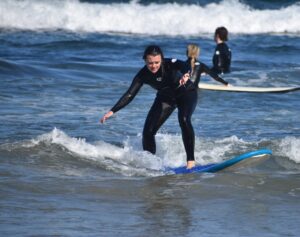 A female student in a black wetsuit surfs on the beach on a sunny day. 