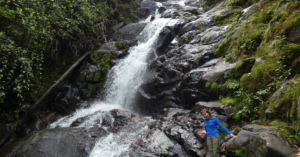 Student in blue raincoat capturing a photo at the base of a waterfall.