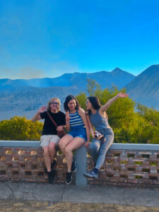 Three friends sit on a ledge with a mountain prominently in the background.