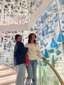 Two students smile for a photo while standing on a staircase in a museum.