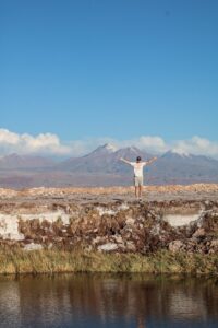 A student standing on a natural rock with his arms spread wide open and facing the mountains in front of him