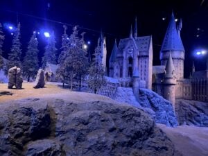 A caled version of the exterior of the Hogwarts castle at Harry Potter Studios in London is lit in hues of dark blue and black. The building is snowy and looks like a magical winter wonderland.