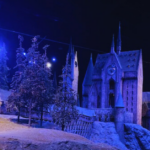 A caled version of the exterior of the Hogwarts castle at Harry Potter Studios in London is lit in hues of dark blue and black. The building is snowy and looks like a magical winter wonderland.