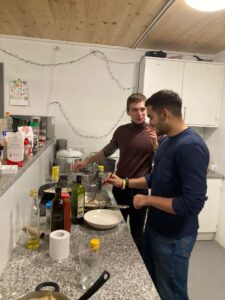 Two friends cook in a student kitchen. The kitchen is white with a granite countertop.