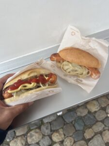 Two sausages in fluffy bread buns. One sausage has ketchup and the other has onions. 