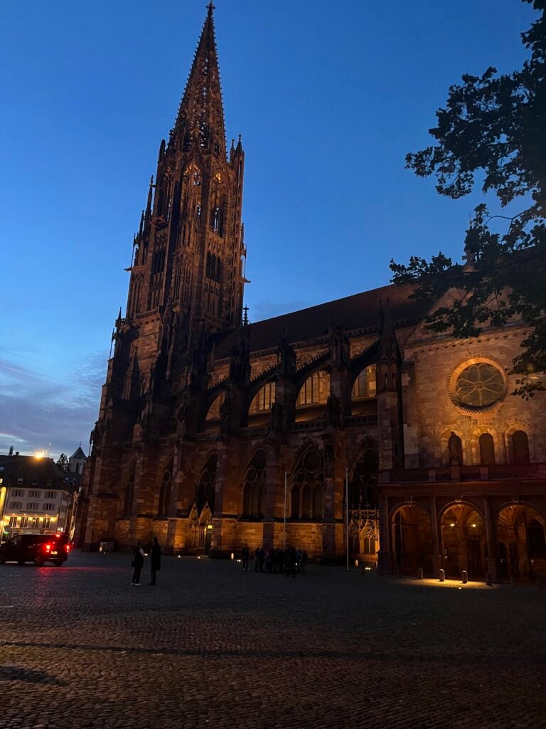 A historical building is illuminated the color of an orange sunset against a setting blue sky.