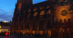 A historical building is illuminated the color of an orange sunset against a setting blue sky.