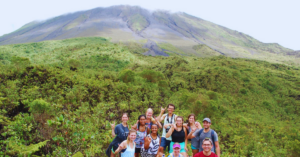 A group of students stands smiling in front of a volano.