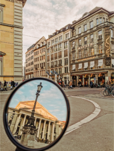 A moped shows historic buildings ahead and behind in the review mirror while in Europe 