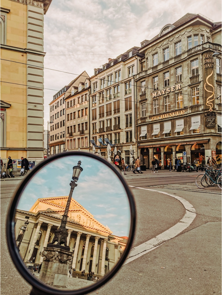 A moped shows historic buildings ahead and behind in the review mirror while in Europe