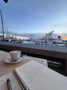 A student is journaling while sitting on a dock and enjoying a cup of hot coffee