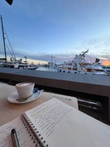 A student is journaling while sitting on a dock and enjoying a cup of hot coffee