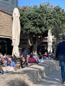 An outdoor plaza in Spain is filled with many people sitting outdoors enjoying the natural air