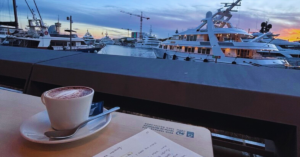 A student is journaling while sitting on a dock and enjoying a cup of hot coffee