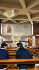 Two male students talk to each other closely while inside a church
