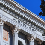 A stunning image of the museo del prado building facade on a bright, sunny day. The building displays several large columns and ancient architecture.
