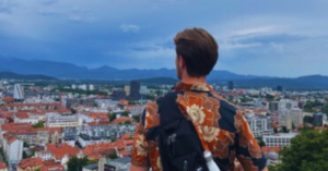 A student's back is in view as the student overlooks many buildings and a mountain range in the distance.