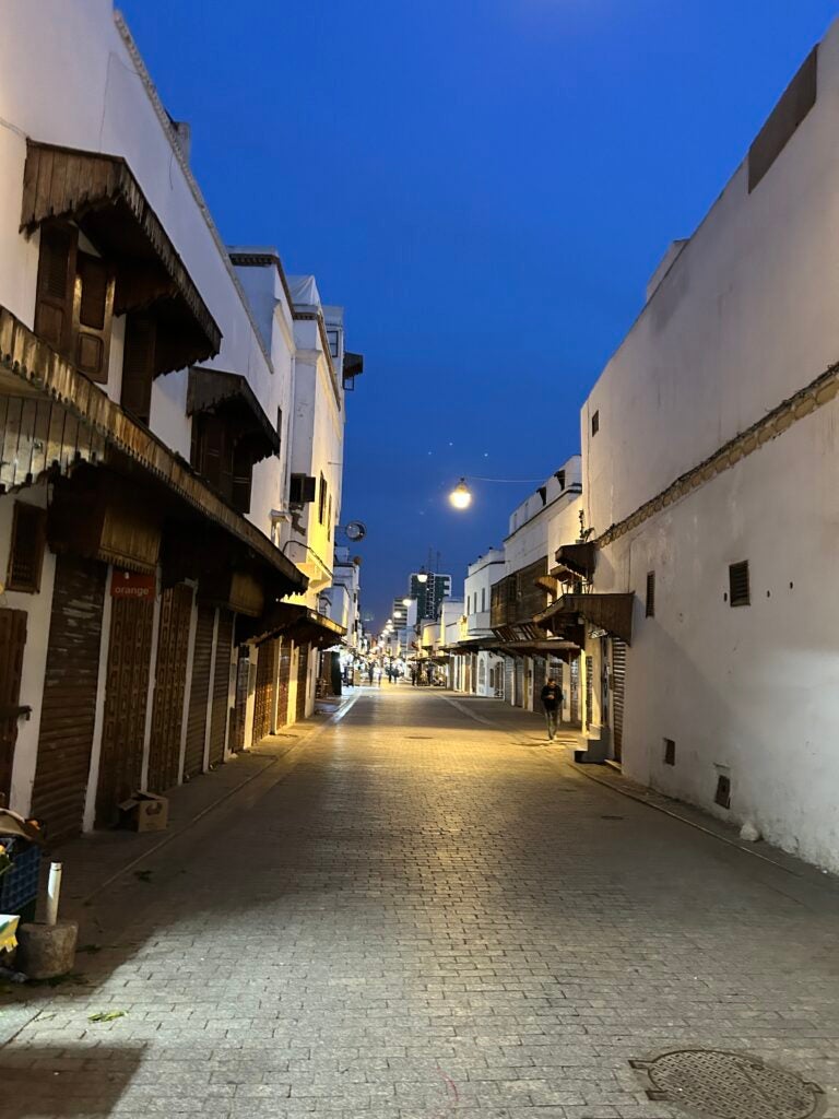 The streets of Morocco are quiet as white, two-story buildings made of clay are deserted and they are in focus against the clear, blue sky overhead.