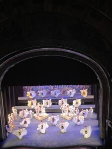 A ballet show with multiple ballet dancers in white costumes and a purple lights fill the stage