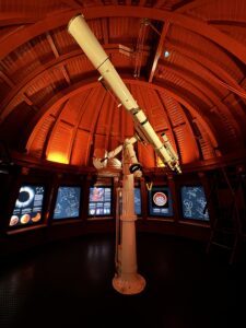The inside roof of a planetarium is hues of red and maroon with a telescope in the center of the dome like room.