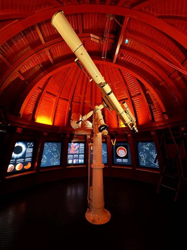 The inside roof of a planetarium is hues of red and maroon with a telescope in the center of the dome like room.