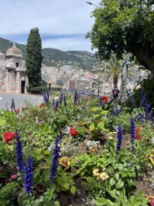 Several Spring flowers bloom in a small urban park with buildings of Italy in the background