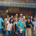 Group of students stand outside of a traditional japanese house