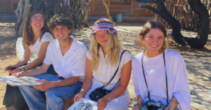 Four students smile at the camera while waiting outdoors