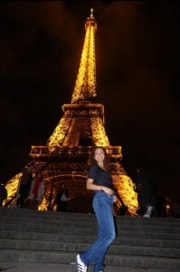 Student standing on the steps side smiling in front of the Eiffel Tower