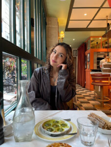 Girl in black jacket sits at a nice restaurant staring shyly at the camera.