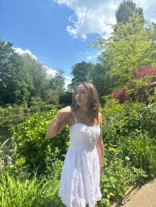 Student in a white dress looks to the side of the camera while visiting a lush garden in France