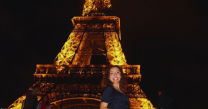 Student standing on the steps side smiling in front of the Eiffel Tower