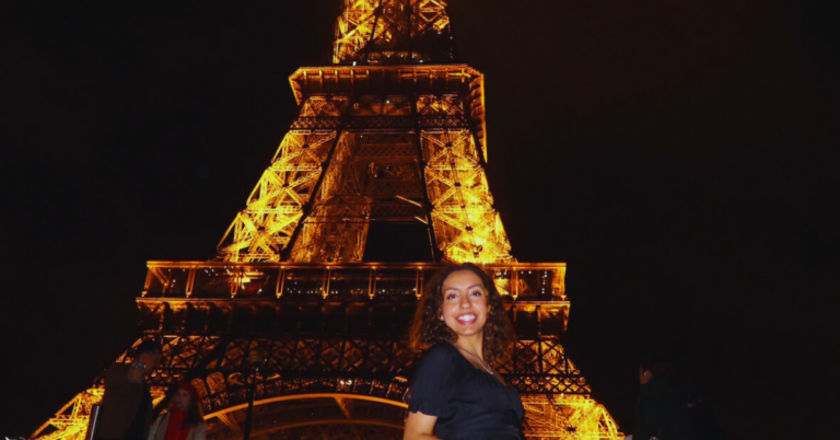 Student standing on the steps side smiling in front of the Eiffel Tower