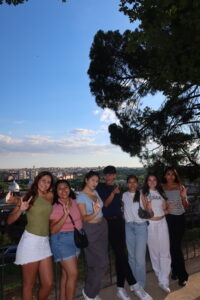 A group of students pose for a camera while outdoors overlooking a city far ahead.