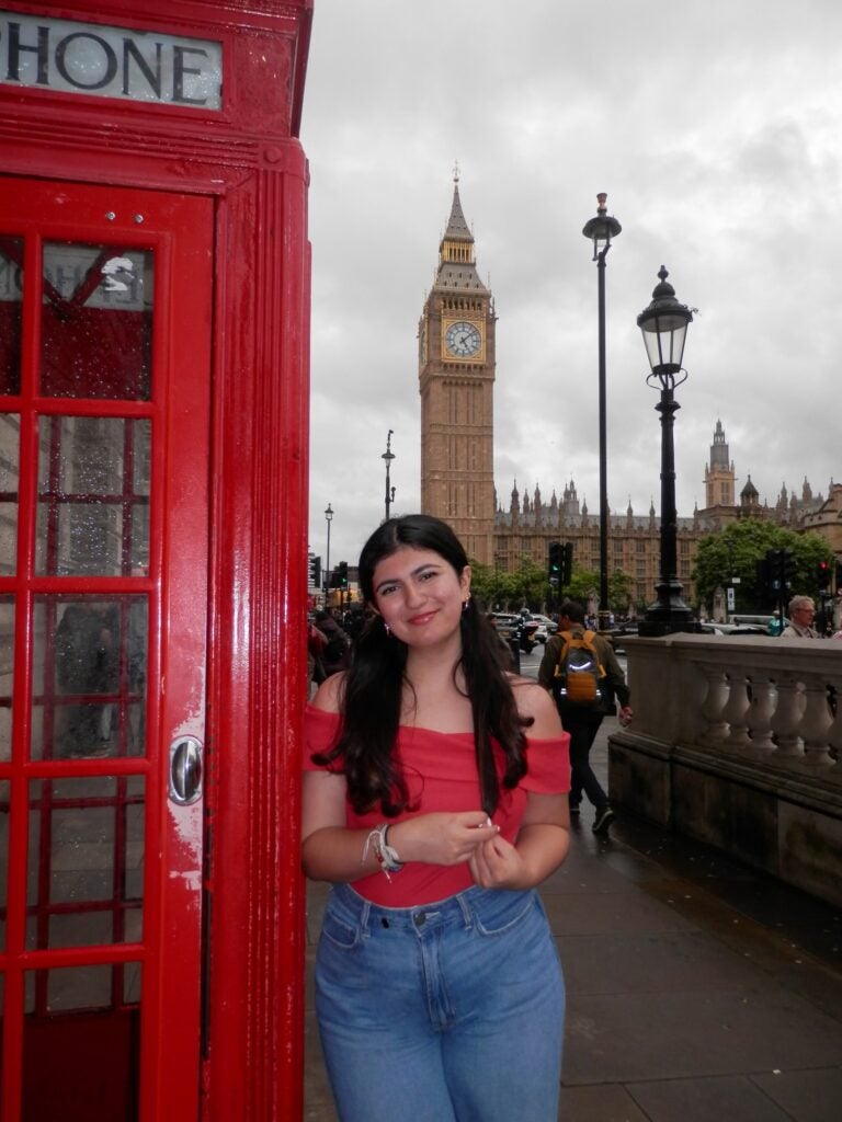 Student smiles as they stand in front of Big Bend and the famous red telephone booth.