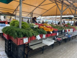 Plastic containers full of fresh herbs and vegetables on display at an open air market