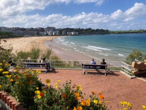 A few people sit on a bench that overlooks a sandy beach.