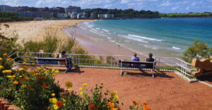 A few people sit on a bench that overlooks a sandy beach.