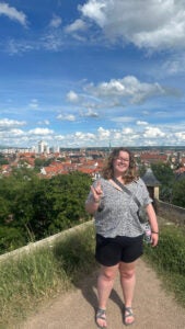 Student holding up the UT hand symbol with orange stucco roof tops behind her.