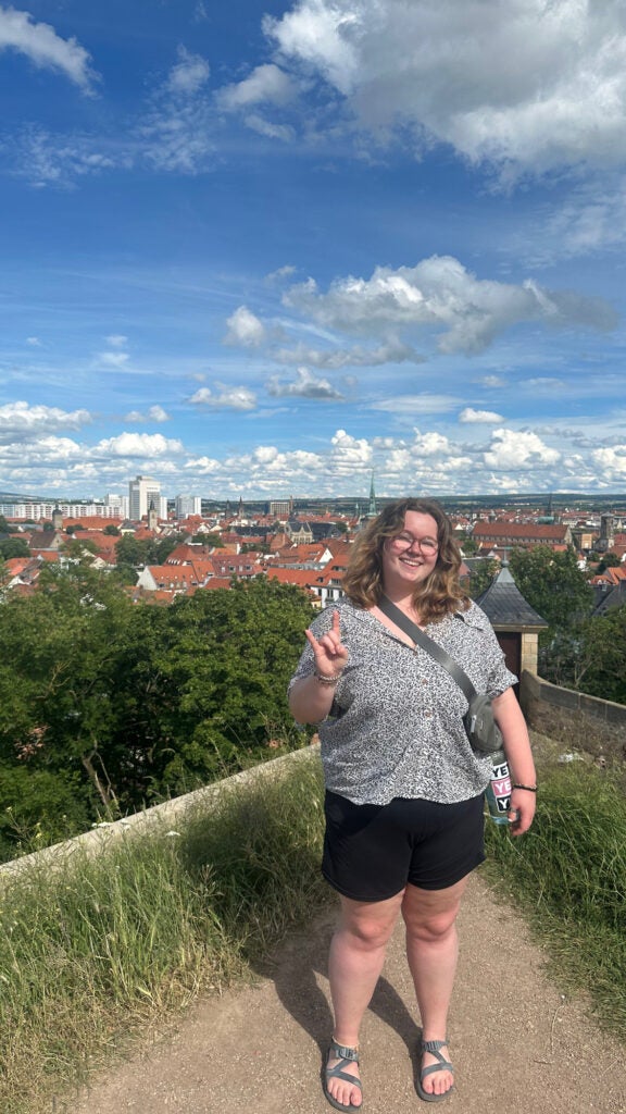 Student holding up the UT hand symbol with orange stucco roof tops behind her.