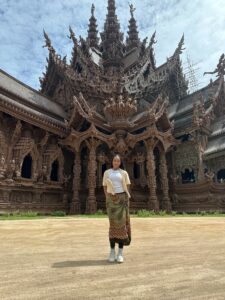 A student smiles in front of a brown, gothic Asian structure.