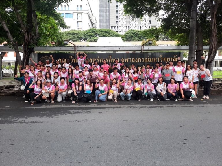 A group of students and teachers wearing pink posing for a group photo outside.