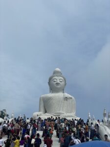 A white Buddha with many people walking up the stairs to get a closer view.