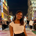 A student smiles directly at the camera in front of a bustling street in South Korea.