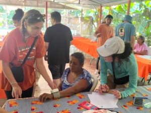 A group of two students stand on either side of a woman getting her blood pressure checked at an outdoor health fair