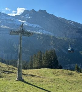 A view beside the gondola in Kandersteg - green hills and pine trees give way to tall snow covered mountains in the background