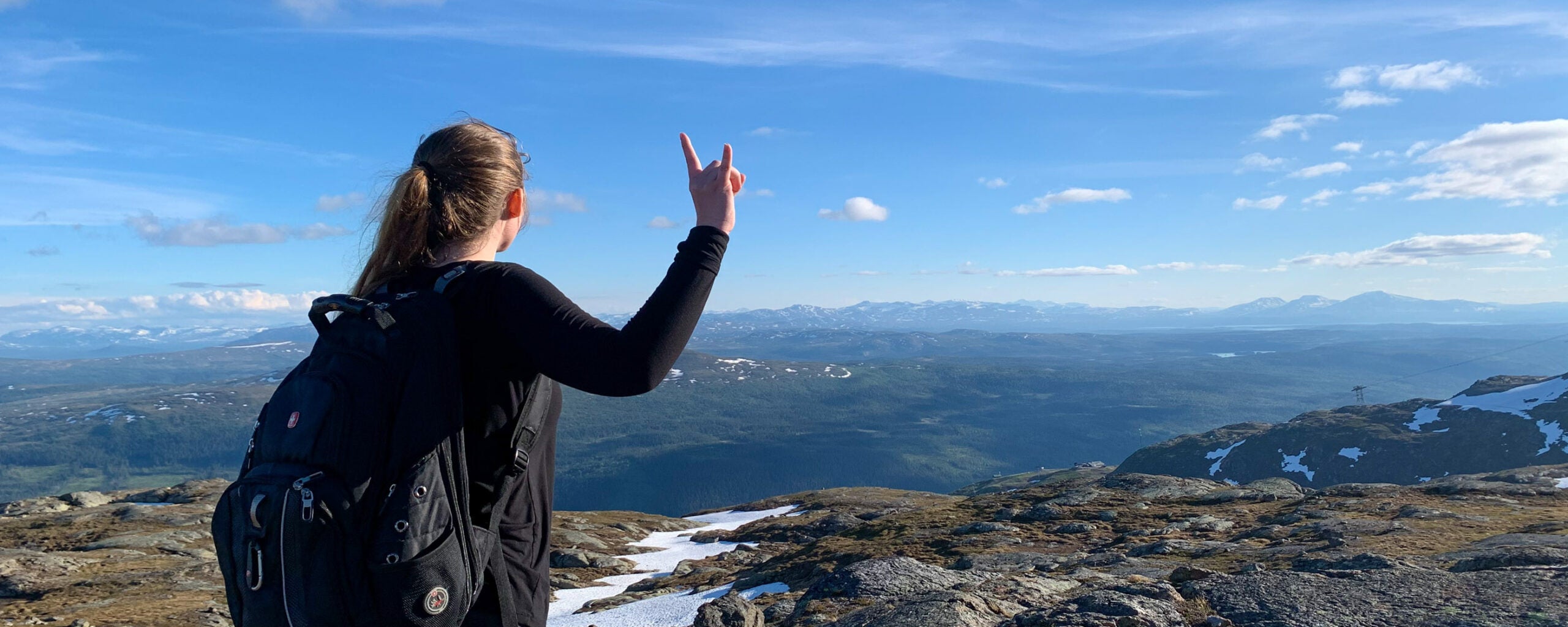 A girl stands at the top of precipice on a beautiful day and shows her Longhorn pride with the Hook'em sign