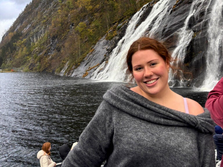 Ava smiles in front a massive watefall from a boat on a cloudy day